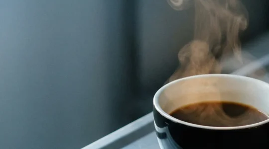 Tasse de café noir abandonnée sur une surface métallique stérile baignée dans une lumière d'aube froide, évoquant le dilemme du jeûne préopératoire